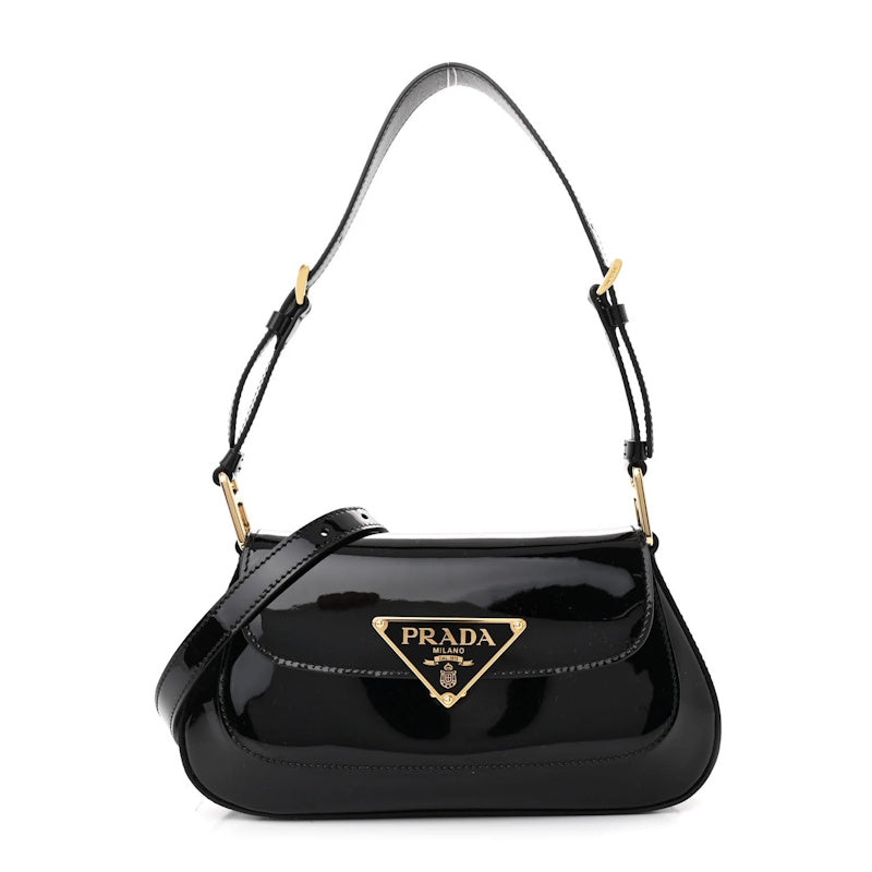 A black patent leather shoulder bag with a gold-tone triangular logo plaque on the front flap, set against a plain white background.