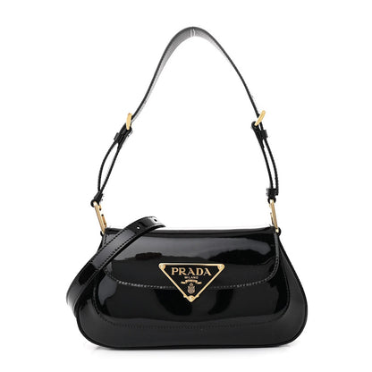 A black patent leather shoulder bag with a gold-tone triangular logo plaque on the front flap, set against a plain white background.