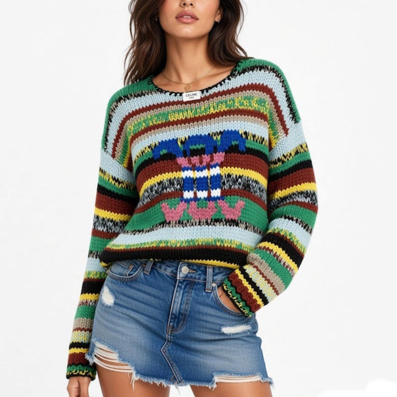A woman modeling a long-sleeve knit sweater with horizontal multicolor stripes and a colorful geometric pattern on the front, paired with a denim mini skirt against a plain white background.