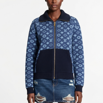 A model wearing a  zip-up jacket featuring a navy blue and light blue monogram pattern, a solid navy ribbed collar, and a solid navy front pocket, paired with a distressed denim skirt against a white studio background.