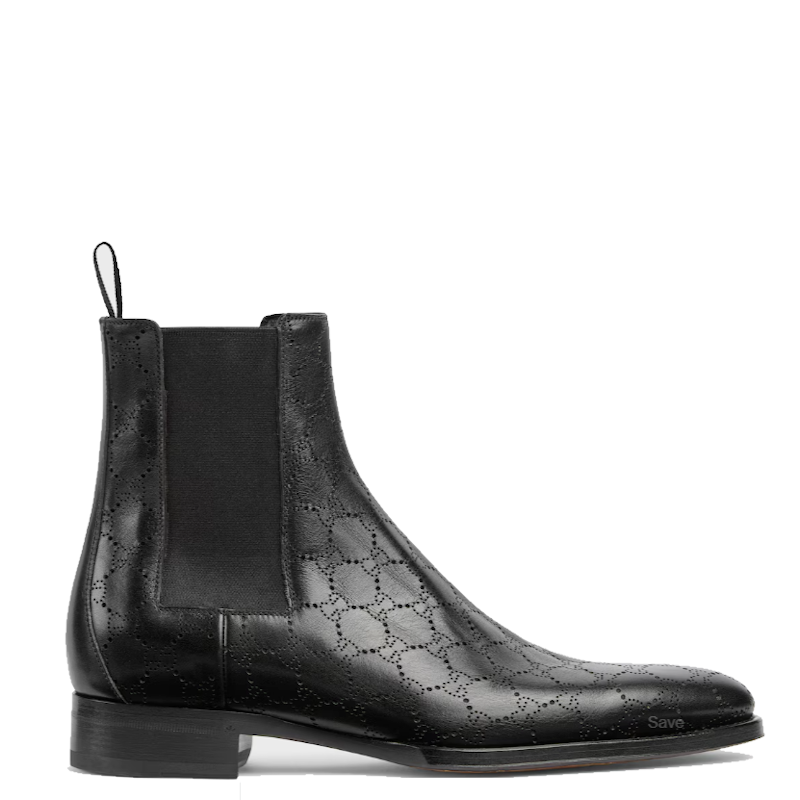 A black leather Chelsea boot with an embossed geometric pattern on the toe and side, a black elastic side panel, and a low stacked heel, shown in profile against a white background.