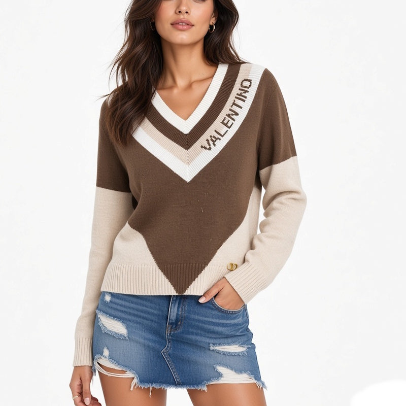A woman wearing a brown and beige color-blocked V-neck sweater with printed on the chest, paired with a distressed denim mini skirt, against a plain white background.