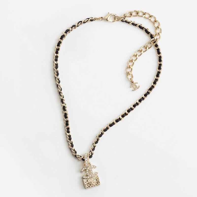 A gold-tone chain necklace featuring a black and gold woven chain design, a small gold-tone pendant with a castle motif, and a matching gold-tone extender chain with a small logo charm, displayed on a clean white background.