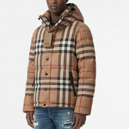 A man wearing a puffer jacket in the brand's signature beige, brown, black, and red check pattern, paired with distressed blue jeans against a plain white background.