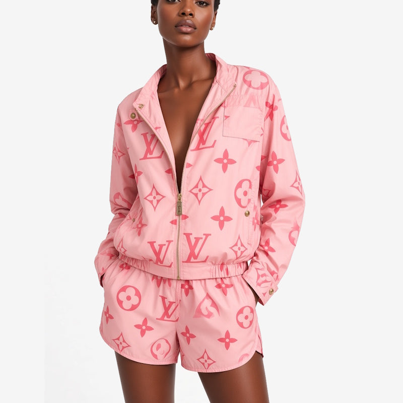 A model wearing a pink monogram zip-up jacket and matching shorts set against a plain light gray studio background.