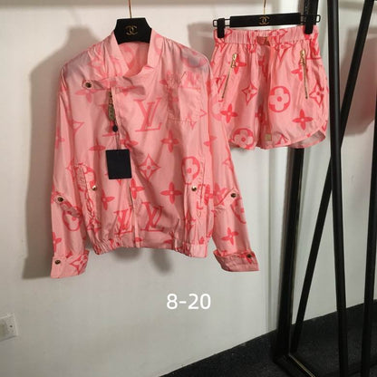 A pink  monogram jacket and matching shorts set hanging on black hangers against a white wall. The set features a light pink base with darker pink LV logos and floral motifs, along with gold-tone hardware.