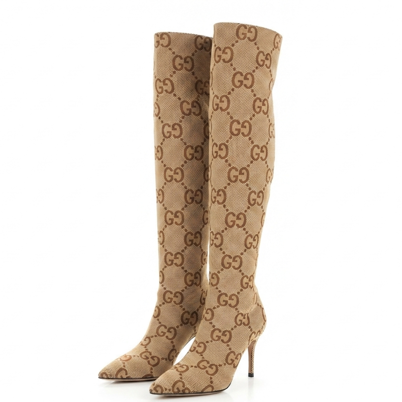 A pair of Gucci knee-high boots in the signature GG monogram canvas, featuring a beige and brown pattern with a pointed toe and slim high heel, set against a plain white background.