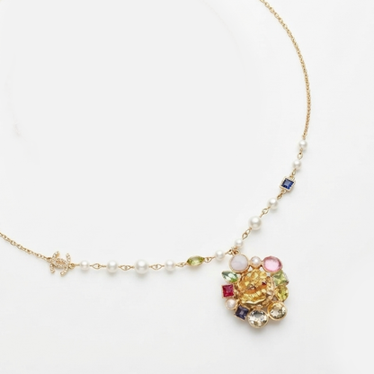 A delicate gold chain necklace featuring small white pearls, a small gold turtle charm, and a colorful floral pendant with yellow, pink, red, and green details, displayed on a clean white background.