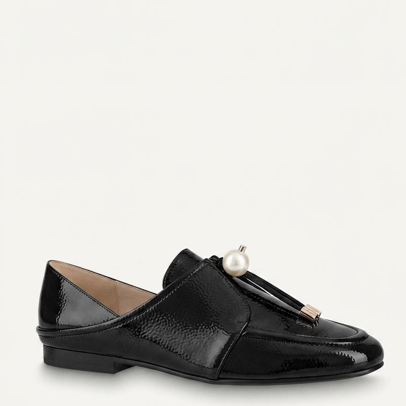 A single black patent leather loafer with a tassel detail featuring a white pearl and a small gold-tone metal accent, shown against a plain off-white background.