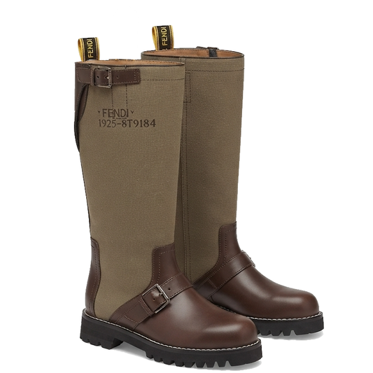 A pair of tall riding boots in olive green canvas and dark brown leather, featuring a buckle strap across the instep and a black lug sole, shown on a white background.