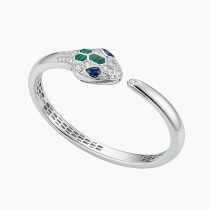A silver snake head ring featuring green and blue stones, set with small clear crystals, on a light gray background.
