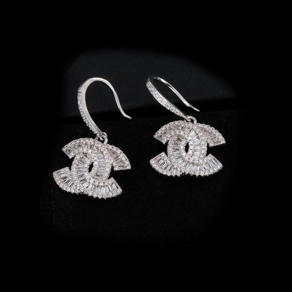 A pair of silver-toned drop earrings featuring a -style interlocking CC motif paved with clear stones, shown on a black background.