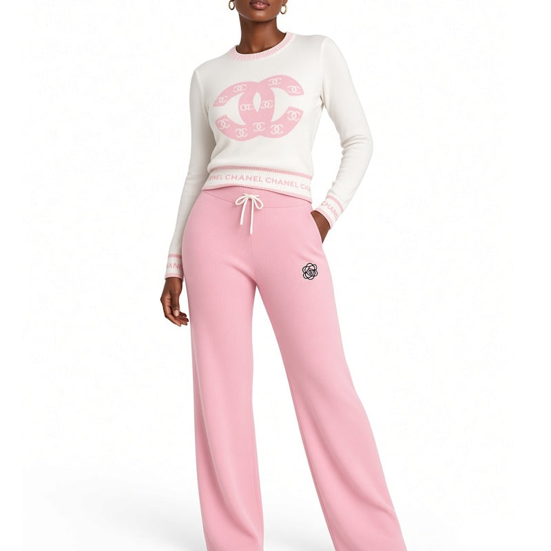 A model wearing a loungewear set consisting of a cream sweatshirt with a pink logo print and pink sweatpants with a drawstring waist, against a plain white background.