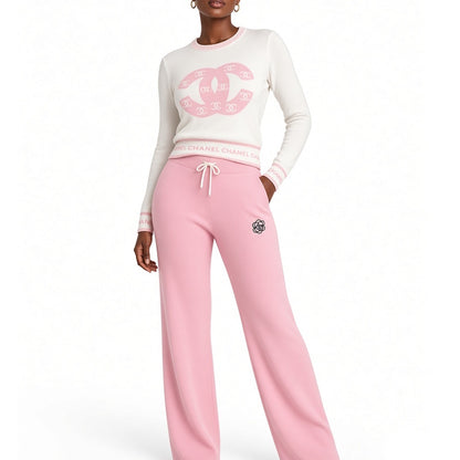 A model wearing a loungewear set consisting of a cream sweatshirt with a pink logo print and pink sweatpants with a drawstring waist, against a plain white background.
