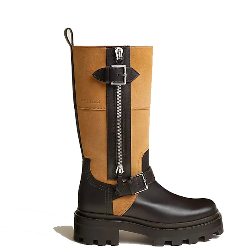 A mid-calf leather boot with a tan suede upper and black leather lower section, featuring a prominent black front zipper with a silver buckle strap and a thick black lug sole.